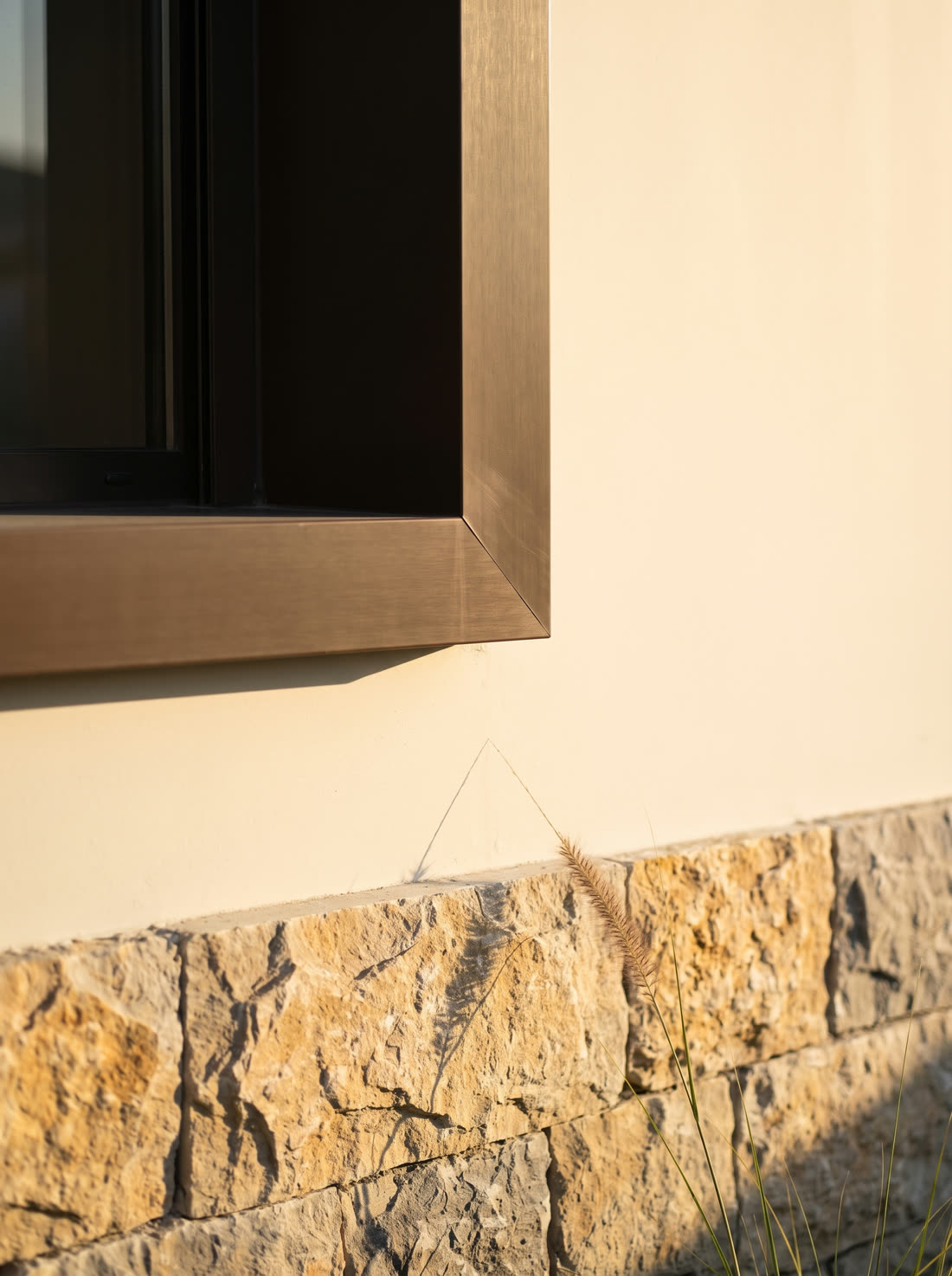 Stone base meeting rendered wall and a bronze window frame